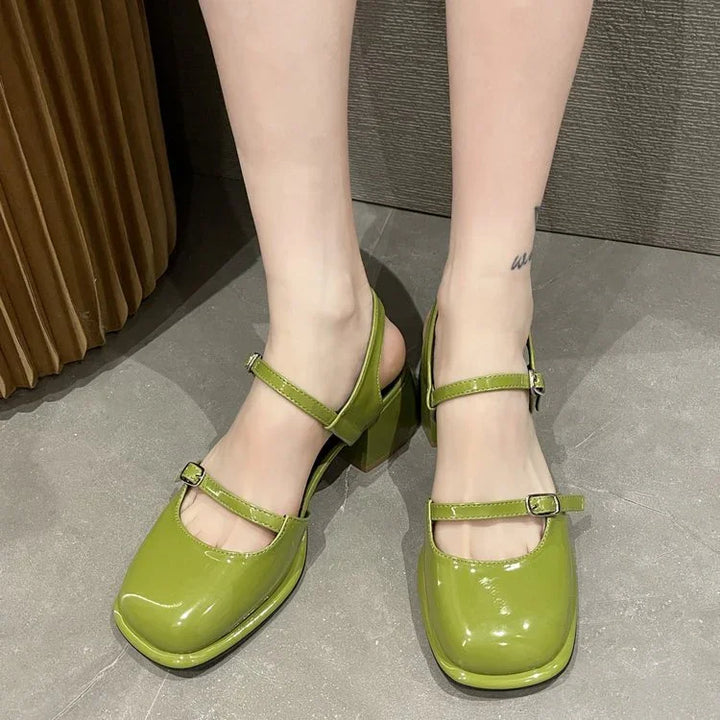 Shiny green patent leather Mary Jane block heel shoes on feet with ankle straps on gray floor