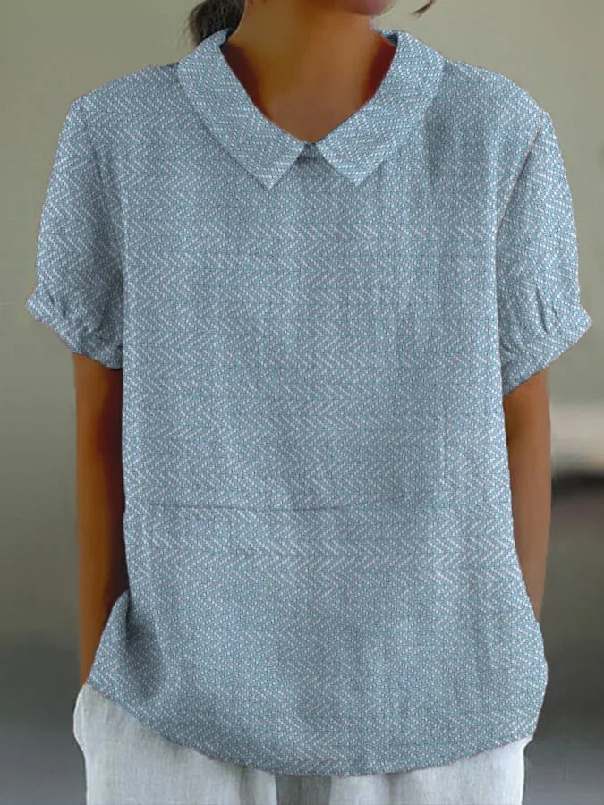 Woman wearing light blue patterned short sleeve blouse with a rounded collar and white pants