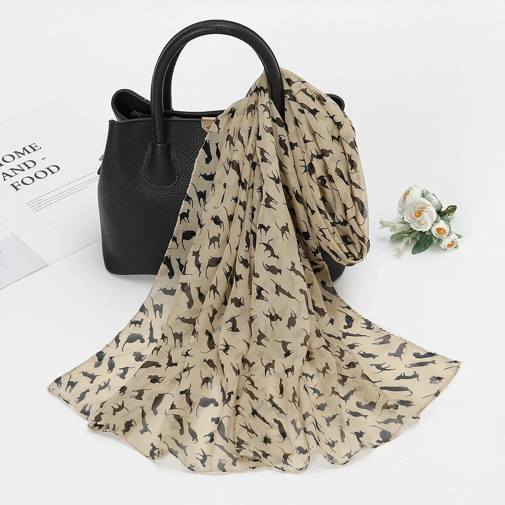 Beige chiffon scarf with black cat silhouettes draped over black leather handbag with flowers and magazine