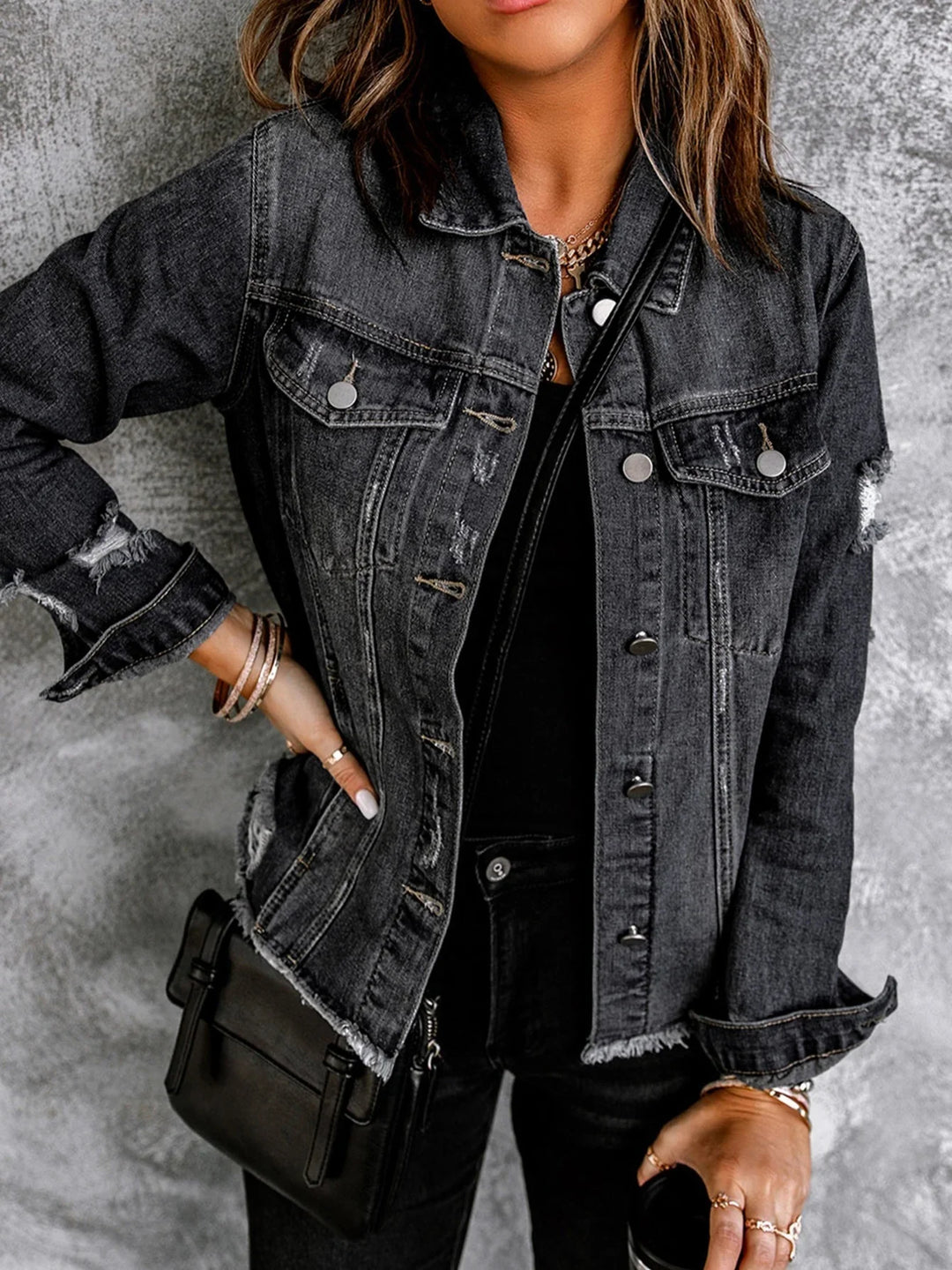 Woman wearing black distressed denim jacket with silver buttons and black crossbody bag