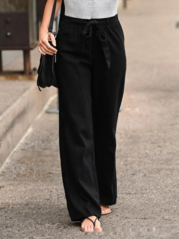 Person wearing black wide-leg pants with waist tie and gray top walking on street