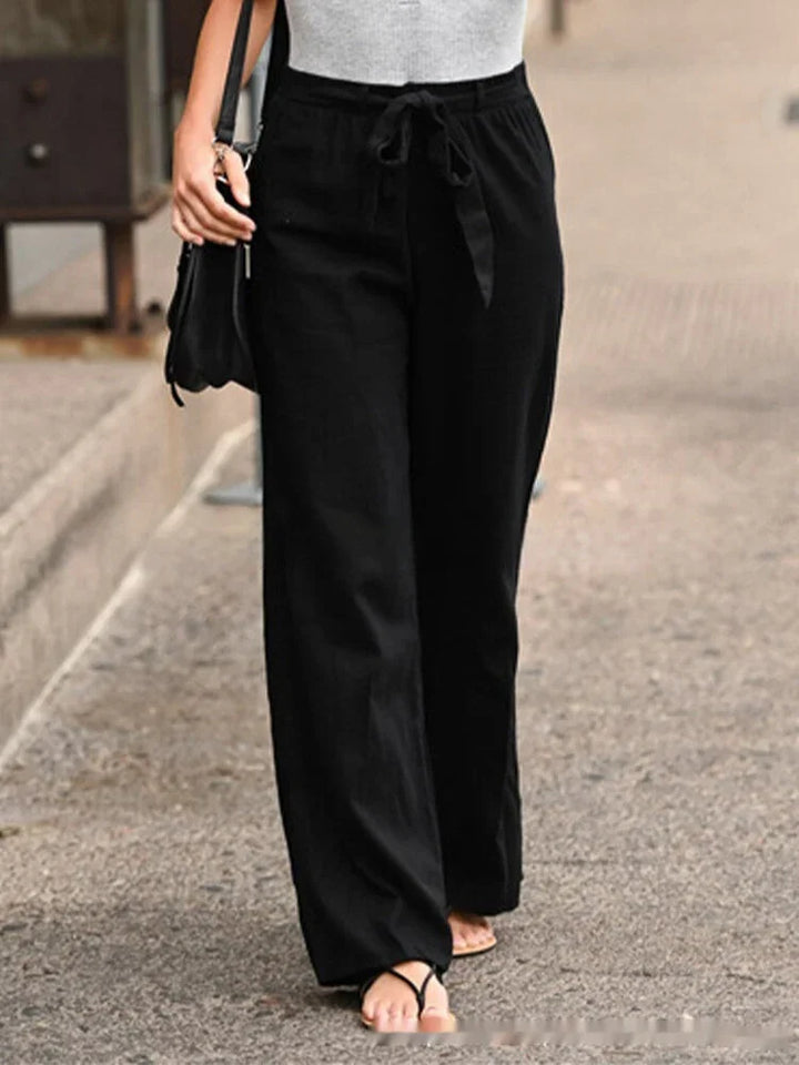 Person wearing black wide-leg pants with waist tie and gray top walking on street