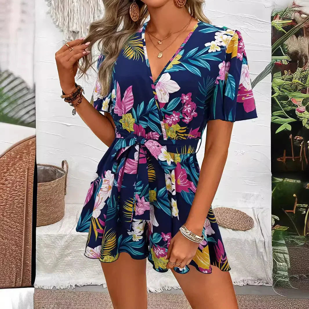 Woman wearing a navy floral short sleeve romper with V-neck and waist tie in a boho indoor setting