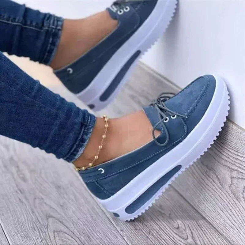 Close-up of blue casual platform sneakers with white soles worn with denim jeans and gold ankle bracelet