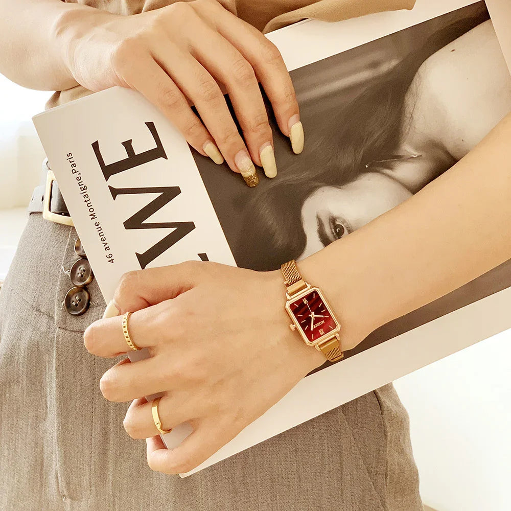 Hands with gold rings and a gold watch holding a fashion magazine featuring a black and white portrait