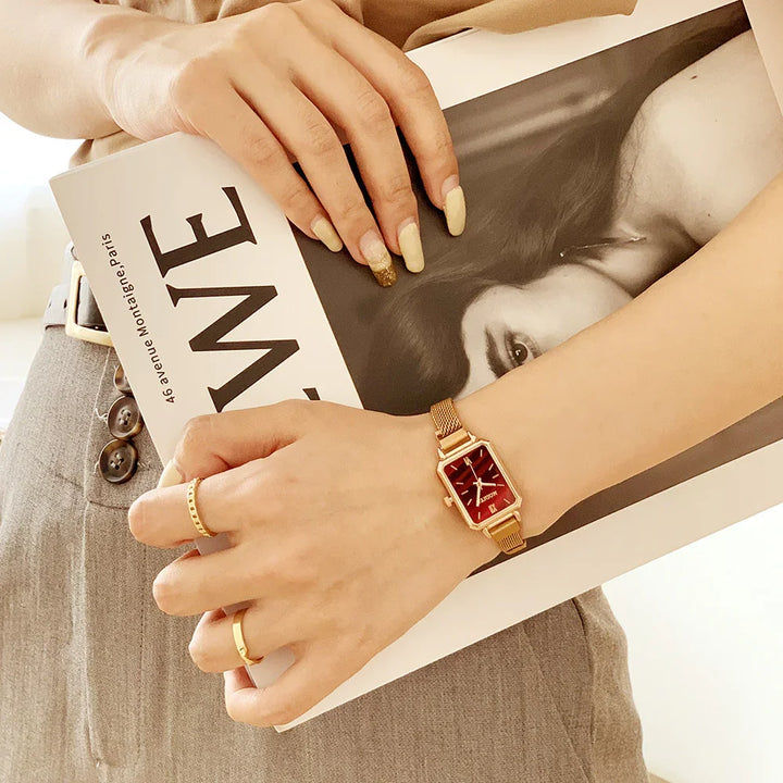 Hands with gold rings and a gold watch holding a fashion magazine featuring a black and white portrait