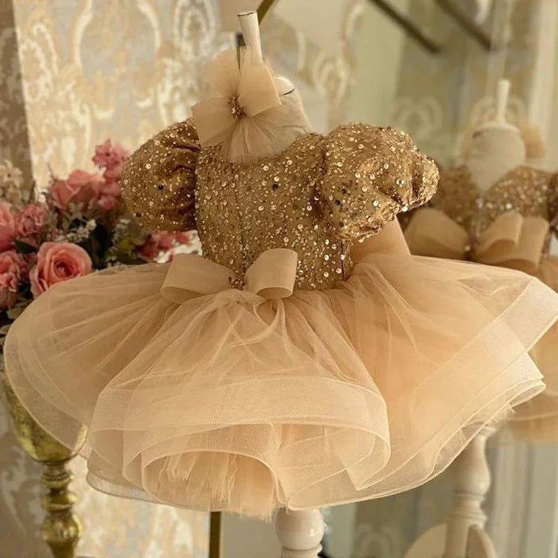 Golden sequin puff sleeve baby dress with layered tulle skirt and bow on mannequin