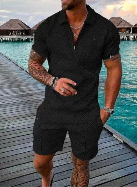 Man wearing black textured short-sleeve shirt and matching shorts on wooden pier by turquoise water