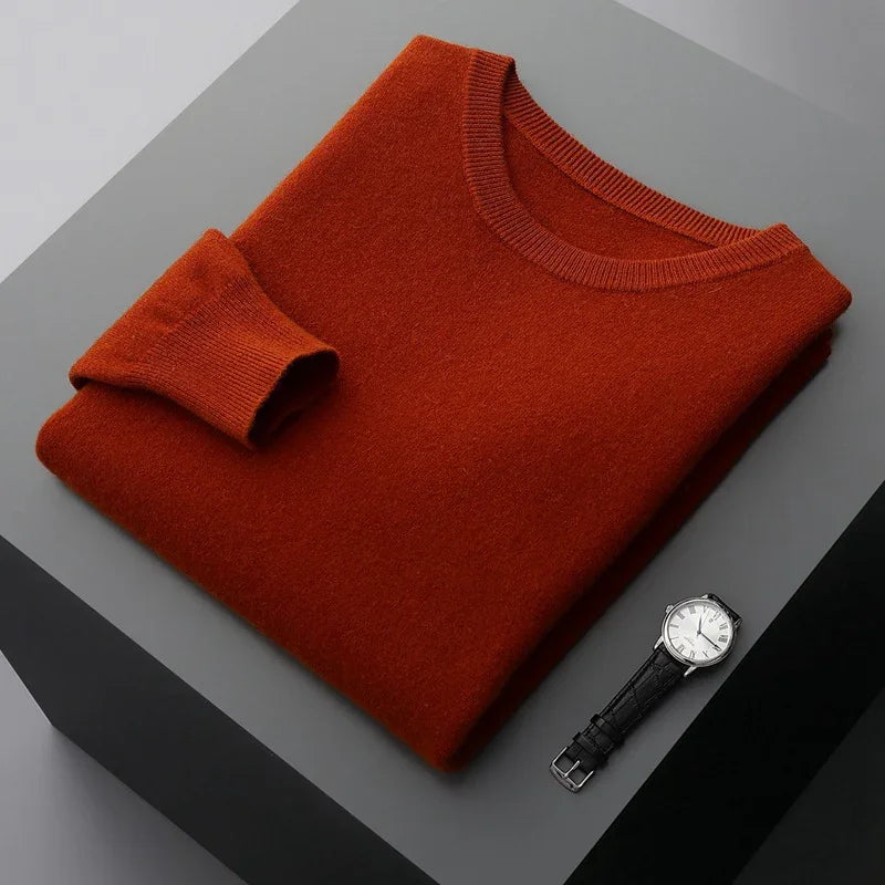 Folded rust orange sweater next to a silver watch with black leather strap on gray surface