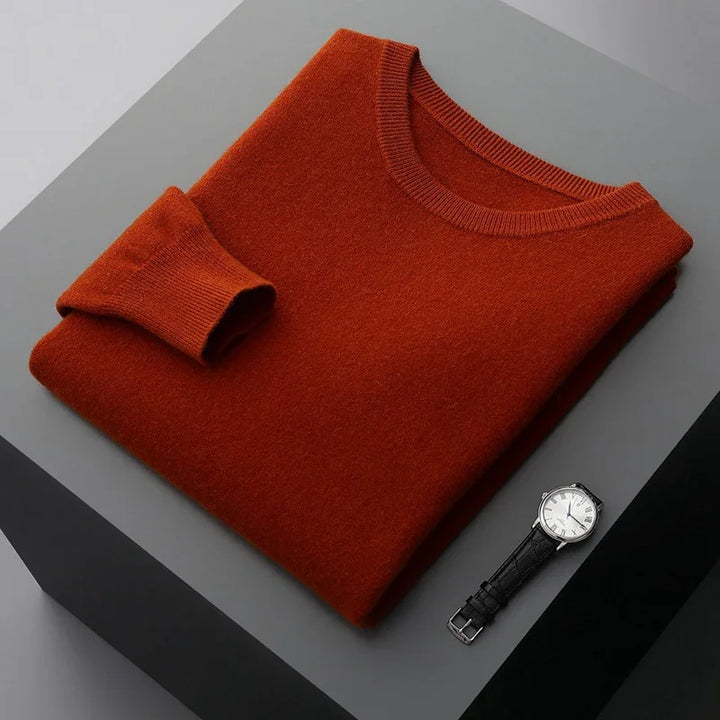 Folded rust orange sweater next to a silver watch with black leather strap on gray surface
