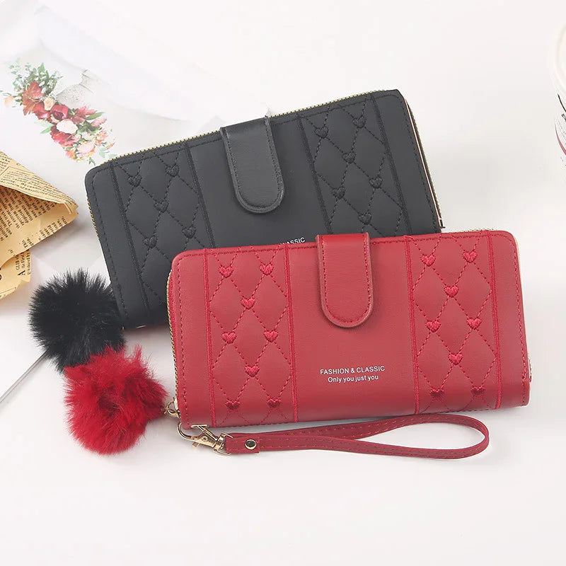 Red and black quilted wristlet wallets with heart patterns and pom-pom keychain on white background