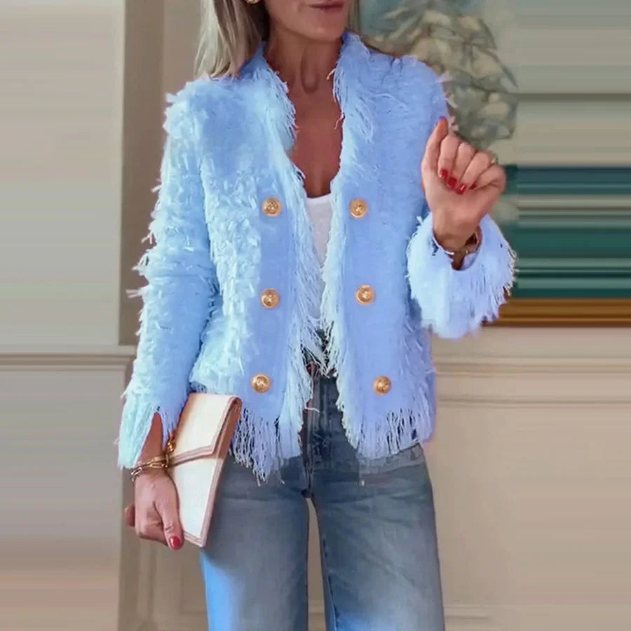 Woman wearing light blue textured fringe blazer with gold buttons, paired with jeans and holding beige clutch