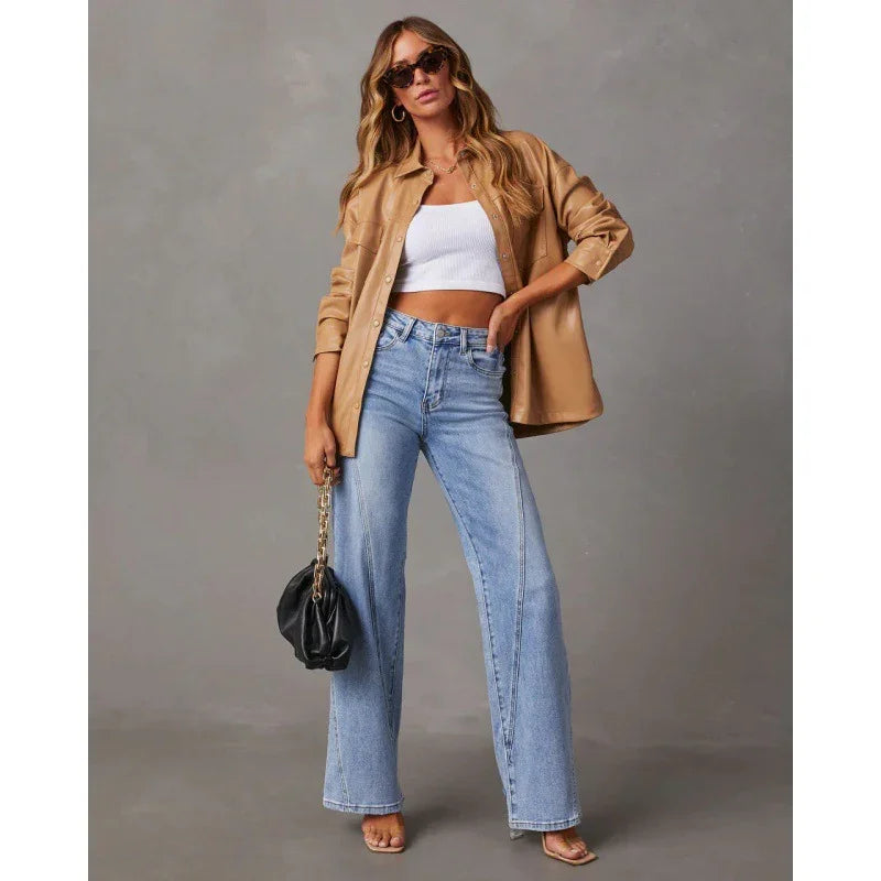 Woman wearing tan button-up jacket, white crop top, wide-leg blue jeans, sunglasses, and holding black handbag