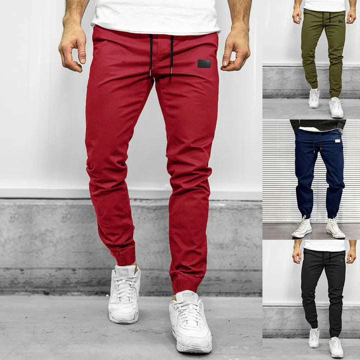 Men's slim fit jogger pants in red, olive green, navy blue, and black with elastic cuffs and white sneakers