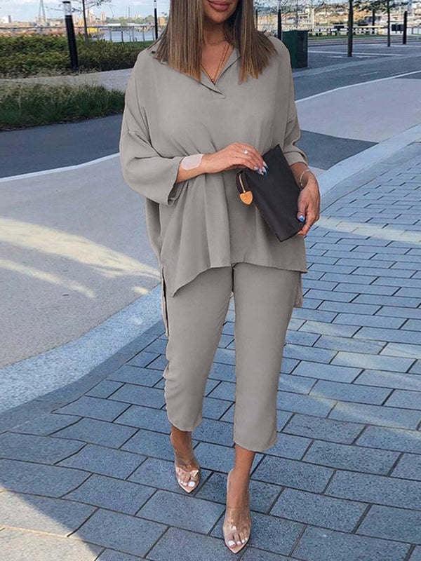 Woman wearing loose beige top and cropped pants walking on city sidewalk with a black clutch