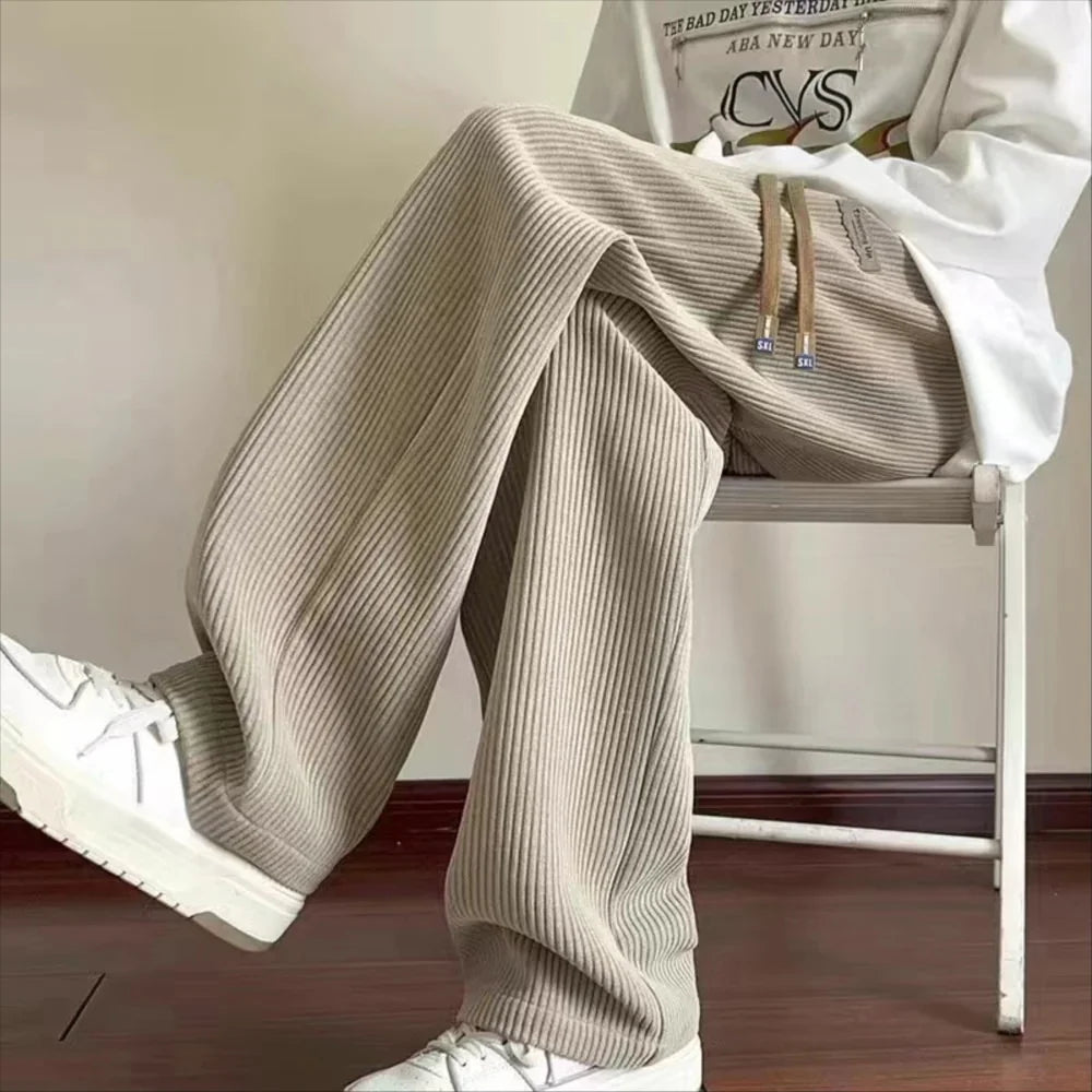 Person wearing beige ribbed knit pants and white sneakers sitting on a white chair indoors