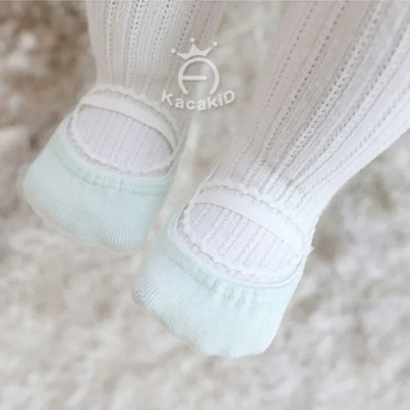 Baby feet wearing white textured tights and mint green soft cotton socks on a fluffy carpet