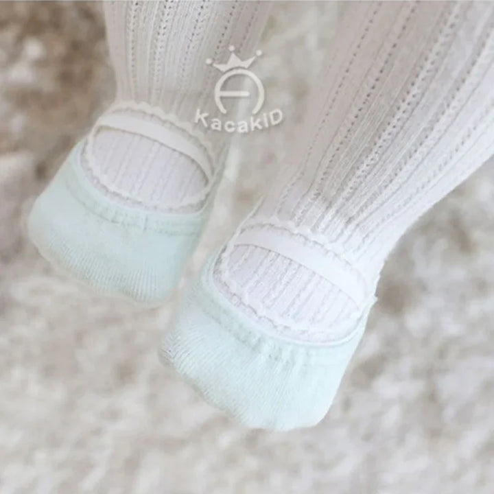 Baby feet wearing white textured tights and mint green soft cotton socks on a fluffy carpet