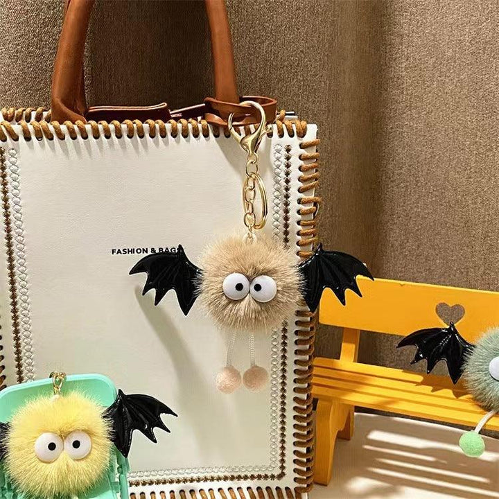 Cute fluffy keychain with big eyes and black bat wings on white leather handbag and yellow bench