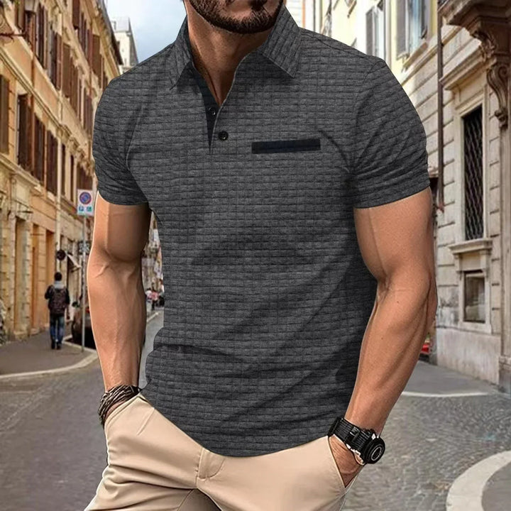 Muscular man wearing dark gray textured polo shirt and beige pants on a cobblestone city street