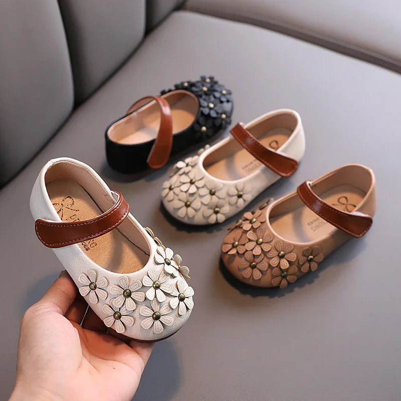 Four pairs of toddler Mary Jane shoes with flower embellishments and brown straps in white, black, beige, and tan colors