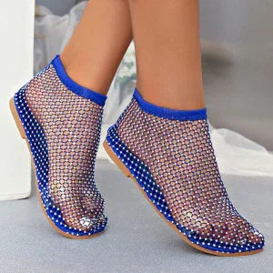 Feet wearing blue mesh water shoes with polka dot soles on a light floor