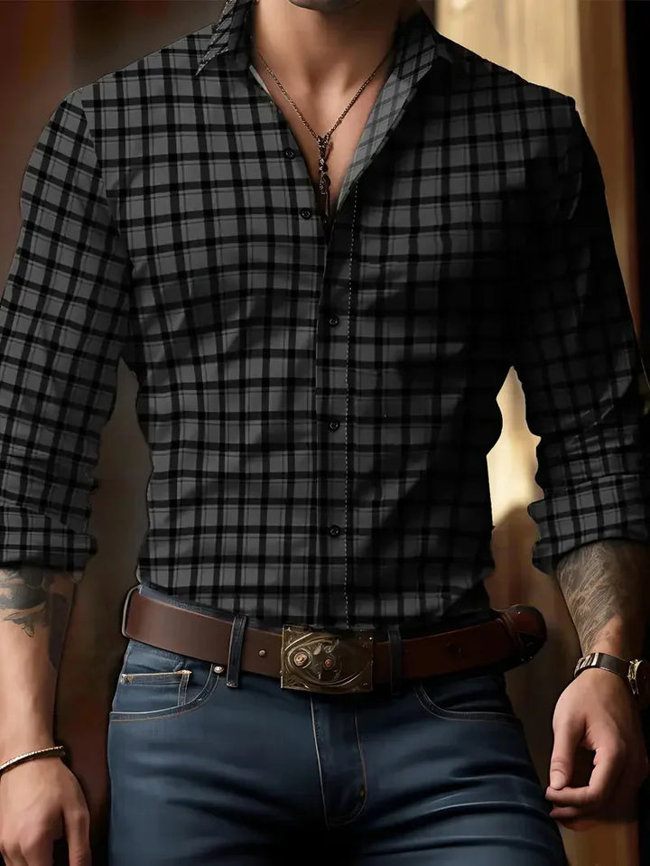 Man wearing black and gray plaid button-up shirt with rolled sleeves, blue jeans, brown belt, and pendant necklace