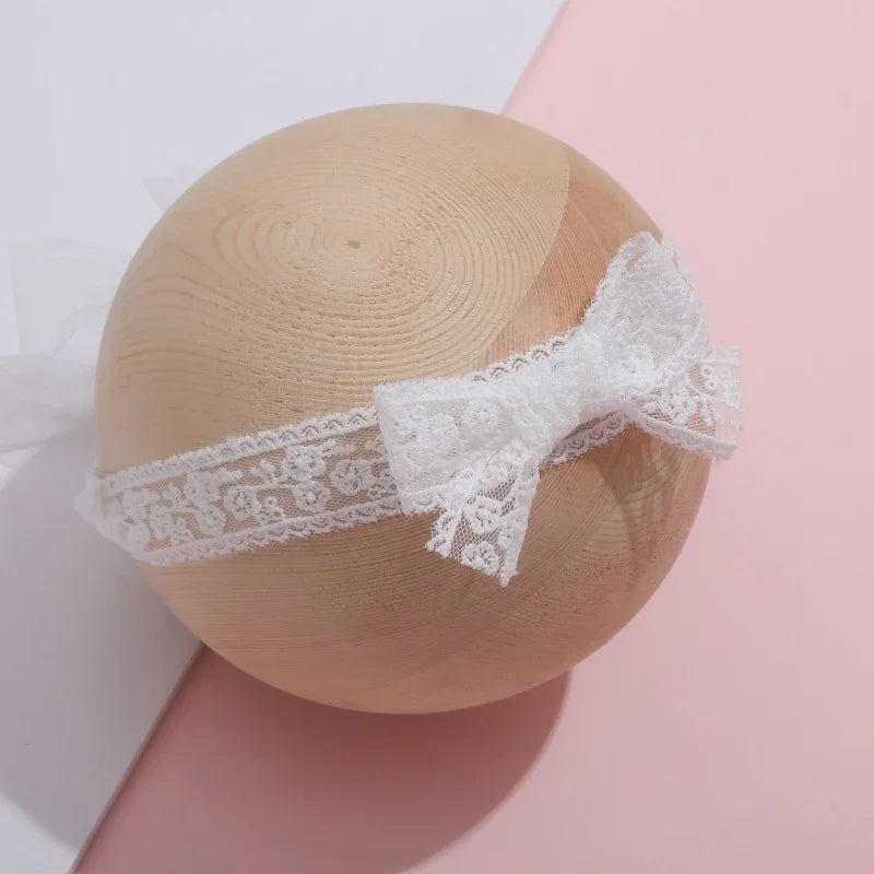 White lace headband with bow displayed on wooden sphere against pink and white background