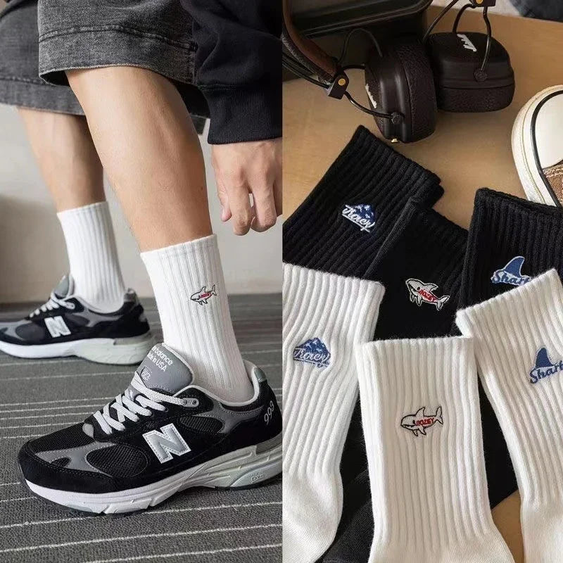 White and black ribbed crew socks with shark and wave embroidery, paired with black New Balance sneakers