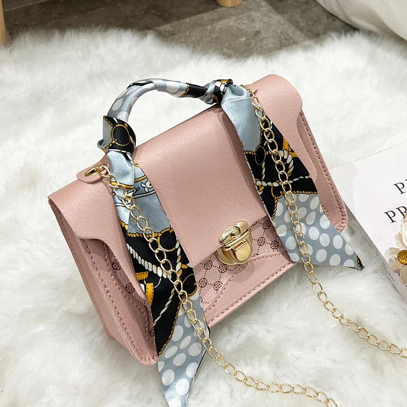 Pink leather handbag with gold clasp, chain strap, and patterned silk scarf handle on white fur