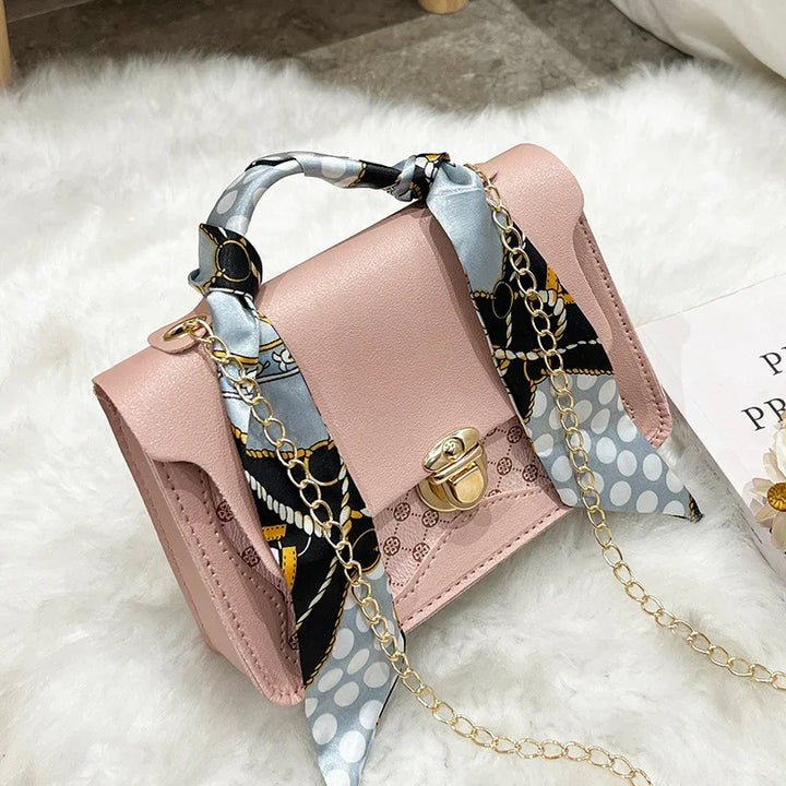 Pink leather handbag with gold clasp, chain strap, and patterned silk scarf handle on white fur