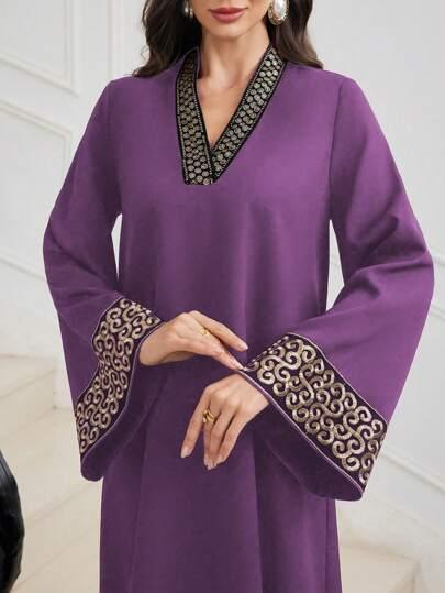 Woman wearing purple dress with black and gold embroidery on V-neck and wide sleeves