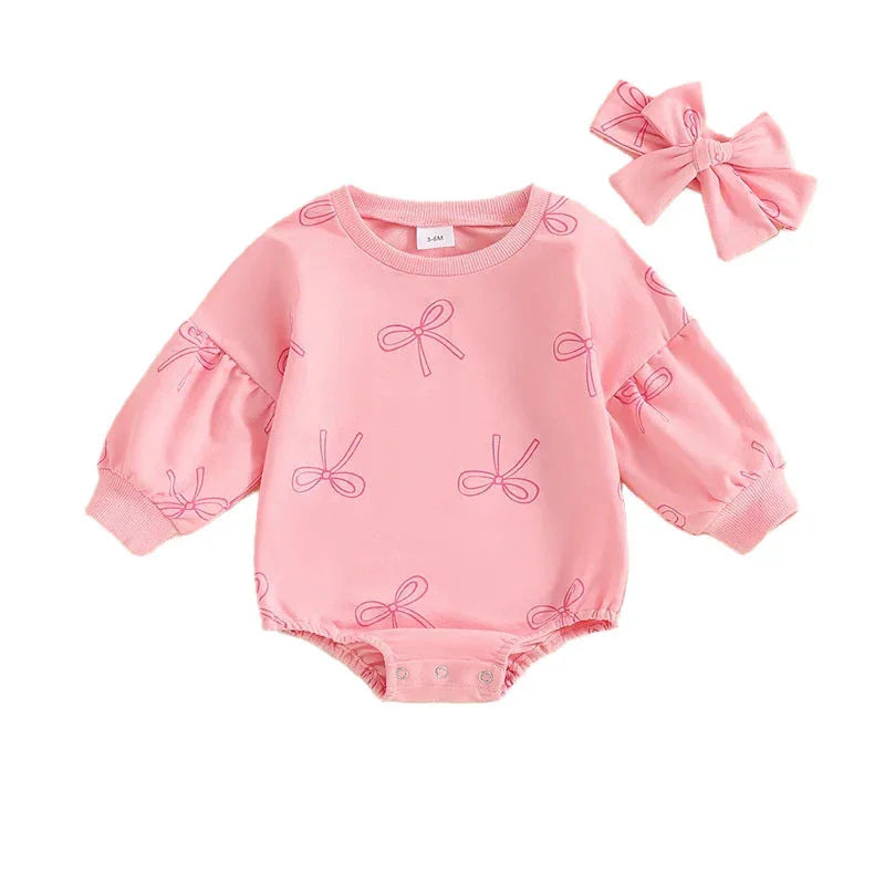 Pink baby romper with long sleeves and bow prints, paired with matching pink bow headband
