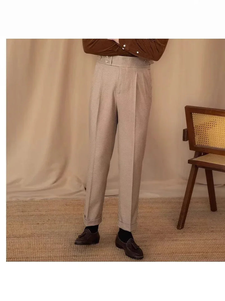 Beige high-waisted pleated trousers paired with black socks and brown tassel loafers in a neutral room