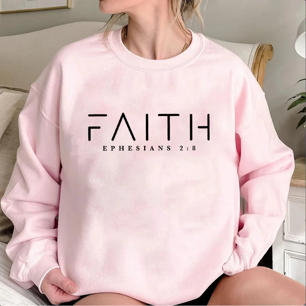 Pink sweatshirt with FAITH and Ephesians 2:8 biblical text, worn by a seated woman indoors