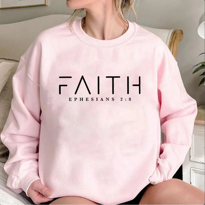 Pink sweatshirt with FAITH and Ephesians 2:8 biblical text, worn by a seated woman indoors