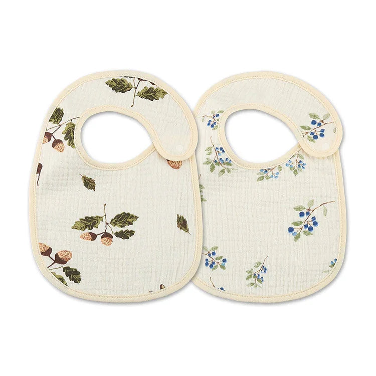 Two cream-colored baby bibs with acorn and blue berry floral prints