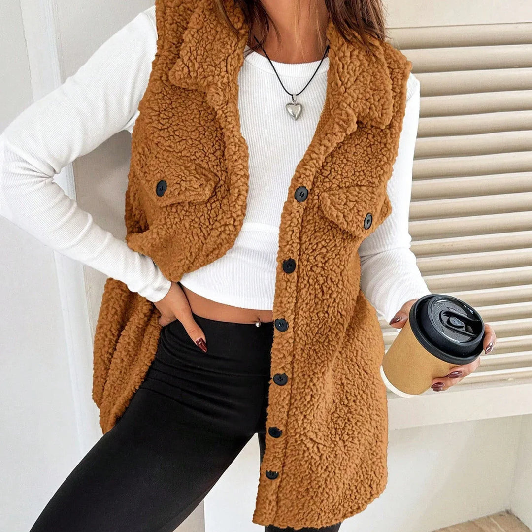 Woman wearing cozy brown sherpa button-up vest, white long-sleeve crop top, black leggings, holding takeaway coffee cup
