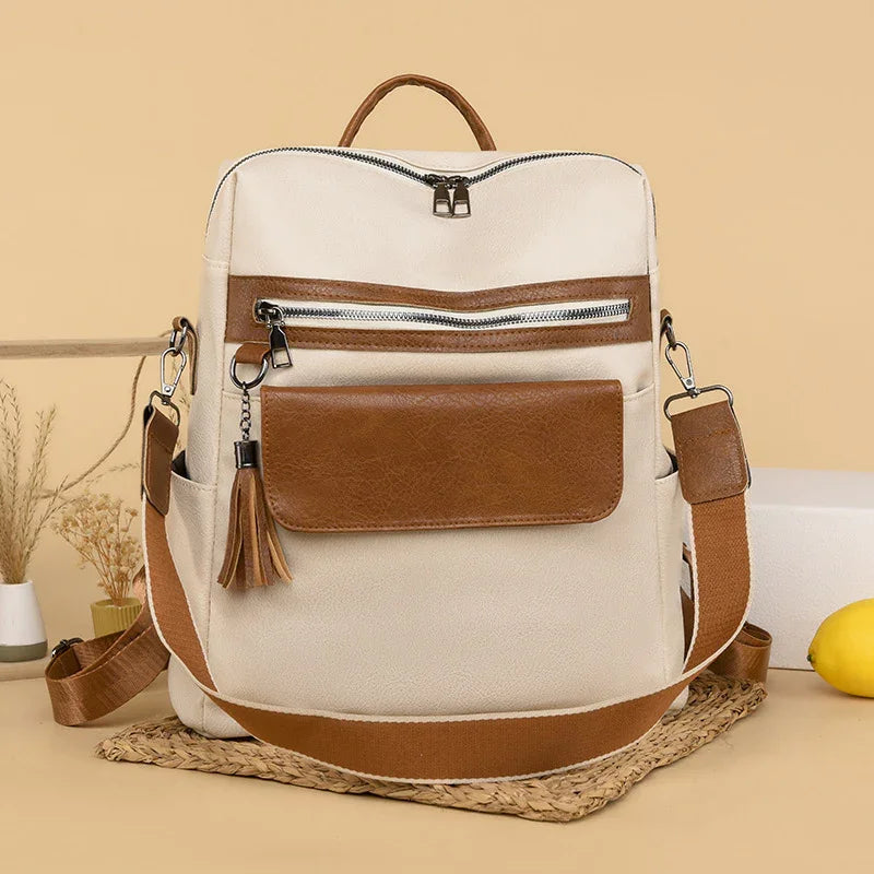 Beige canvas backpack with brown leather pockets, tassel zipper pull, adjustable strap on woven mat