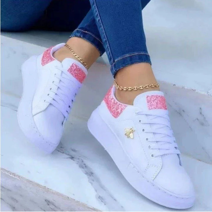 White platform sneakers with pink glitter accents and gold bee charm worn with blue jeans and gold anklets on marble steps