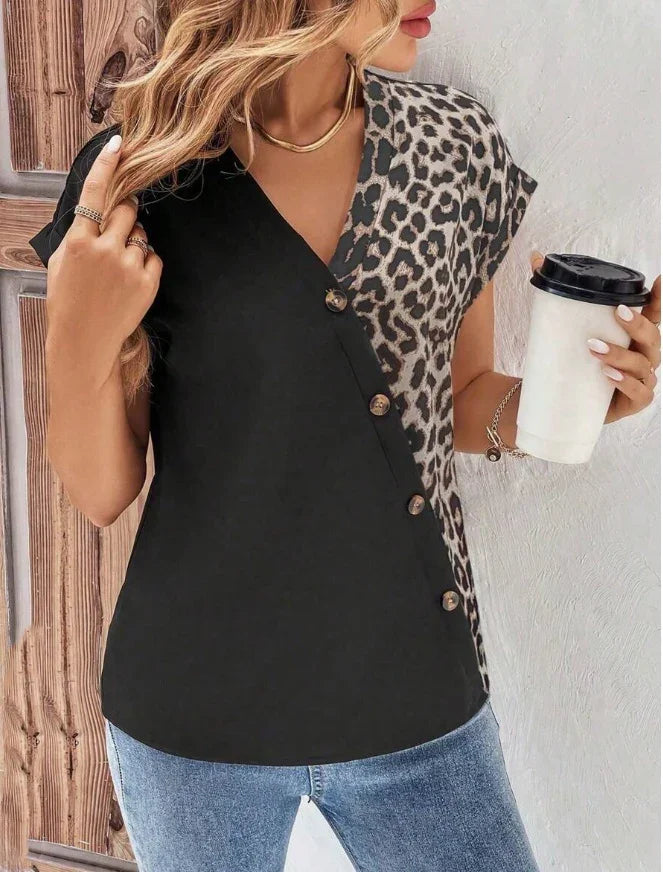 Woman wearing a half leopard print, half black button-up sleeveless top with blue jeans, holding a coffee cup