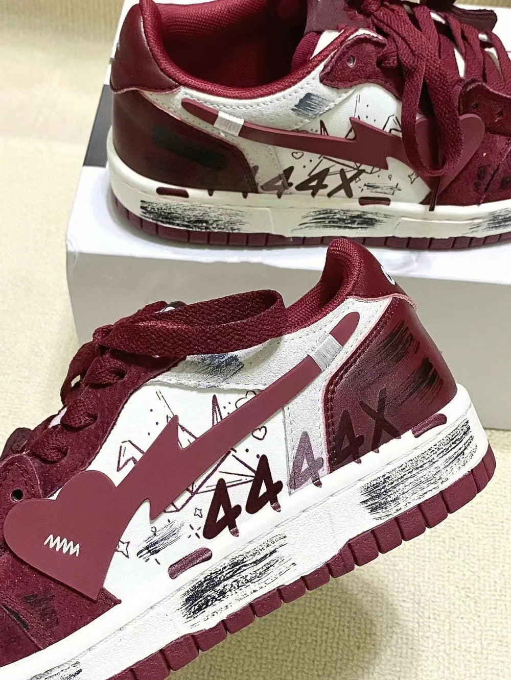 Maroon and white Nike sneakers with lightning bolt swoosh and 444X graffiti design on side