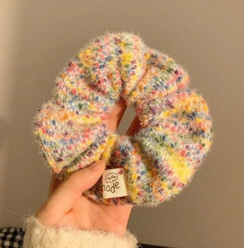 Hand holding a handmade fuzzy multicolor knitted scrunchie with pastel pink, yellow, and blue tones
