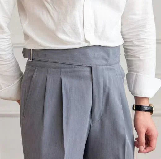 Close-up of high-waisted gray pleated trousers with side buckle, worn with white shirt and black watch