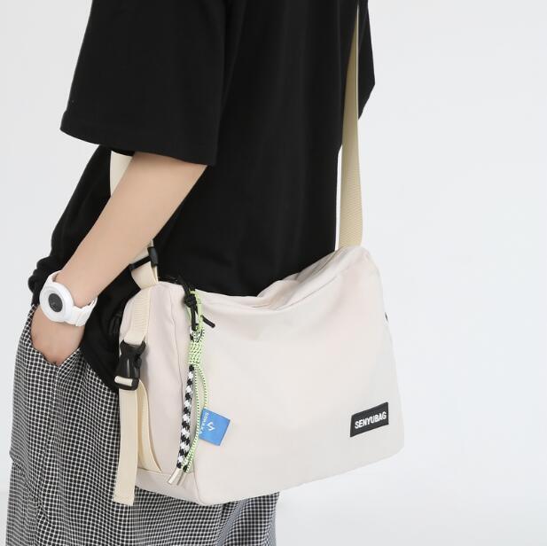Person wearing black shirt and checkered pants carrying a beige SENYUBAG crossbody bag with zipper and decorative cords