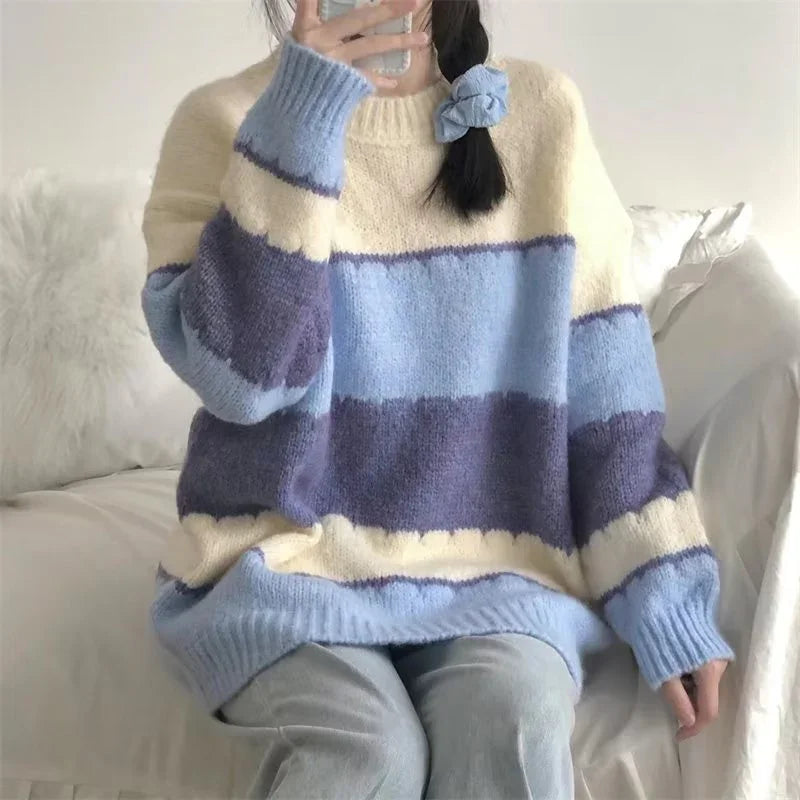 Person wearing cozy oversized striped sweater in cream, light blue, and purple sitting on white sofa