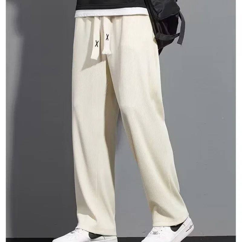 Men's cream ribbed wide-leg sweatpants with drawstring and white Nike sneakers on gray background