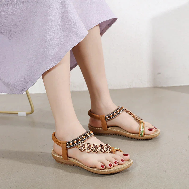 Woman wearing brown beaded flat sandals with ankle straps on a light floor