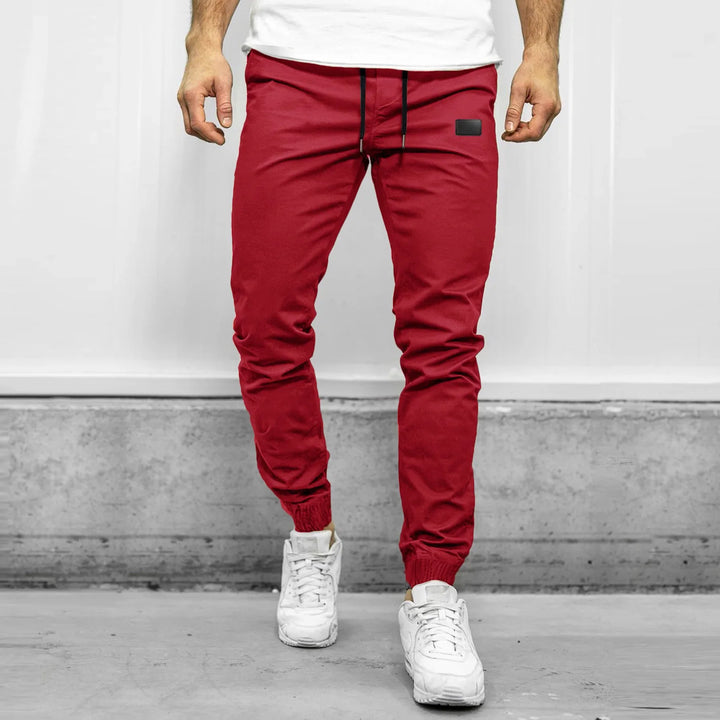 Man wearing slim-fit red jogger pants with drawstring waist and white sneakers in an indoor setting