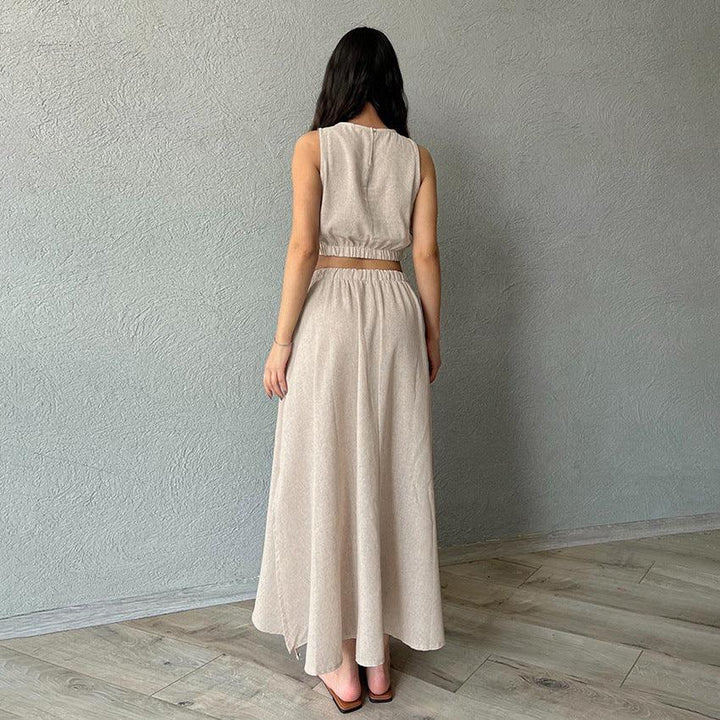 Woman wearing beige sleeveless crop top and long flowing skirt standing on light wooden floor against gray textured wall